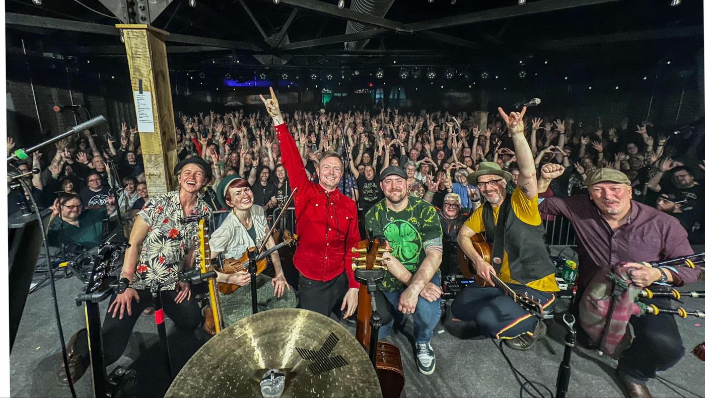 Brian Buchanan and Enter the Haggis onstage in front of a packed crowd, arms raised.